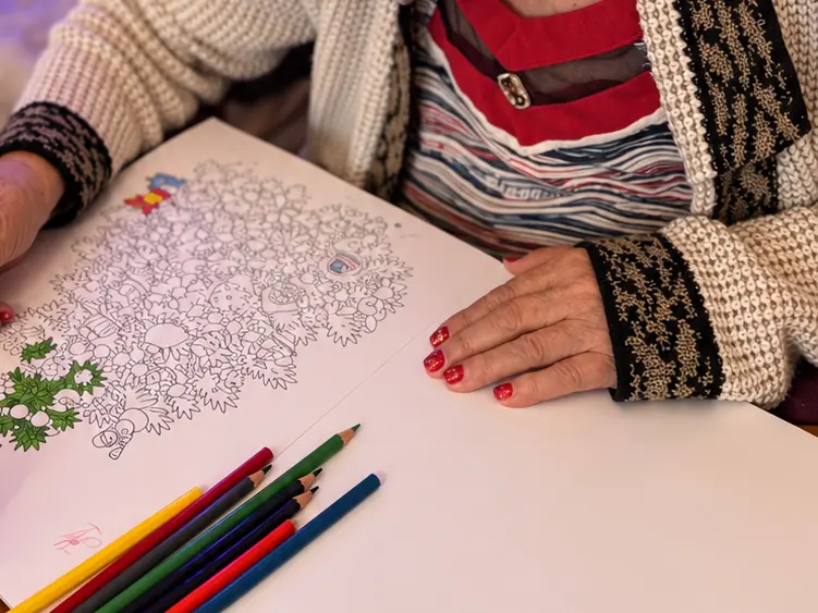 A resident&rsquo;s hands colouring in a picture, with a row of coloured pencils on the table